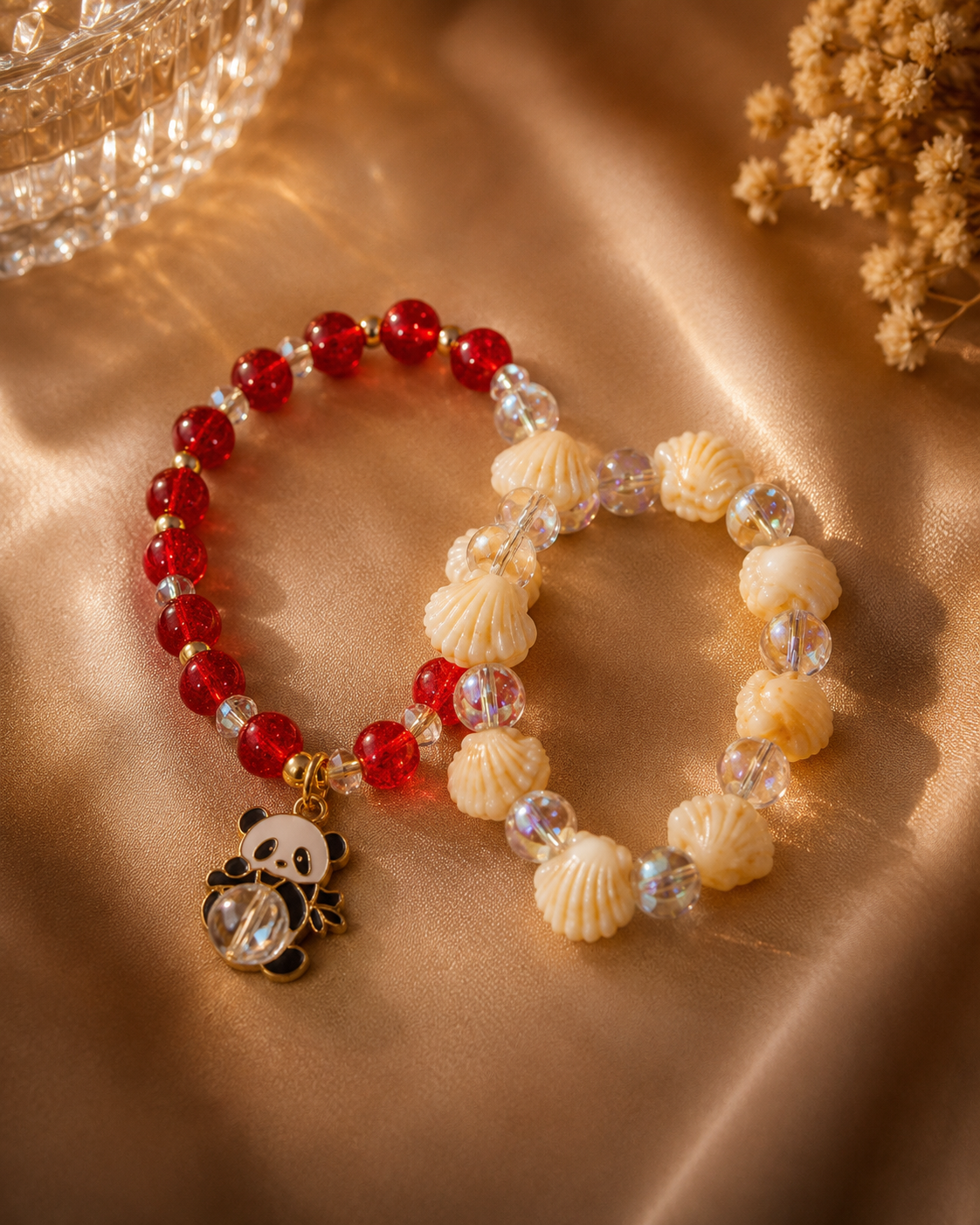 Two beaded bracelets displayed on a warm beige satin background. One bracelet features translucent red beads with a dangling panda charm holding a clear crystal.